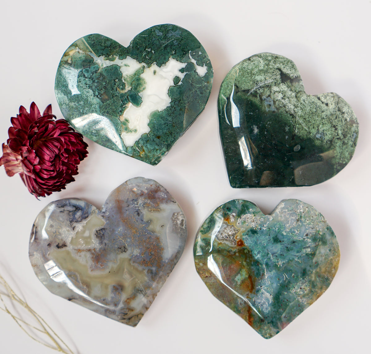 Overhead flat lay of four moss agate heart carvings arranged in a grid with a dried flower
