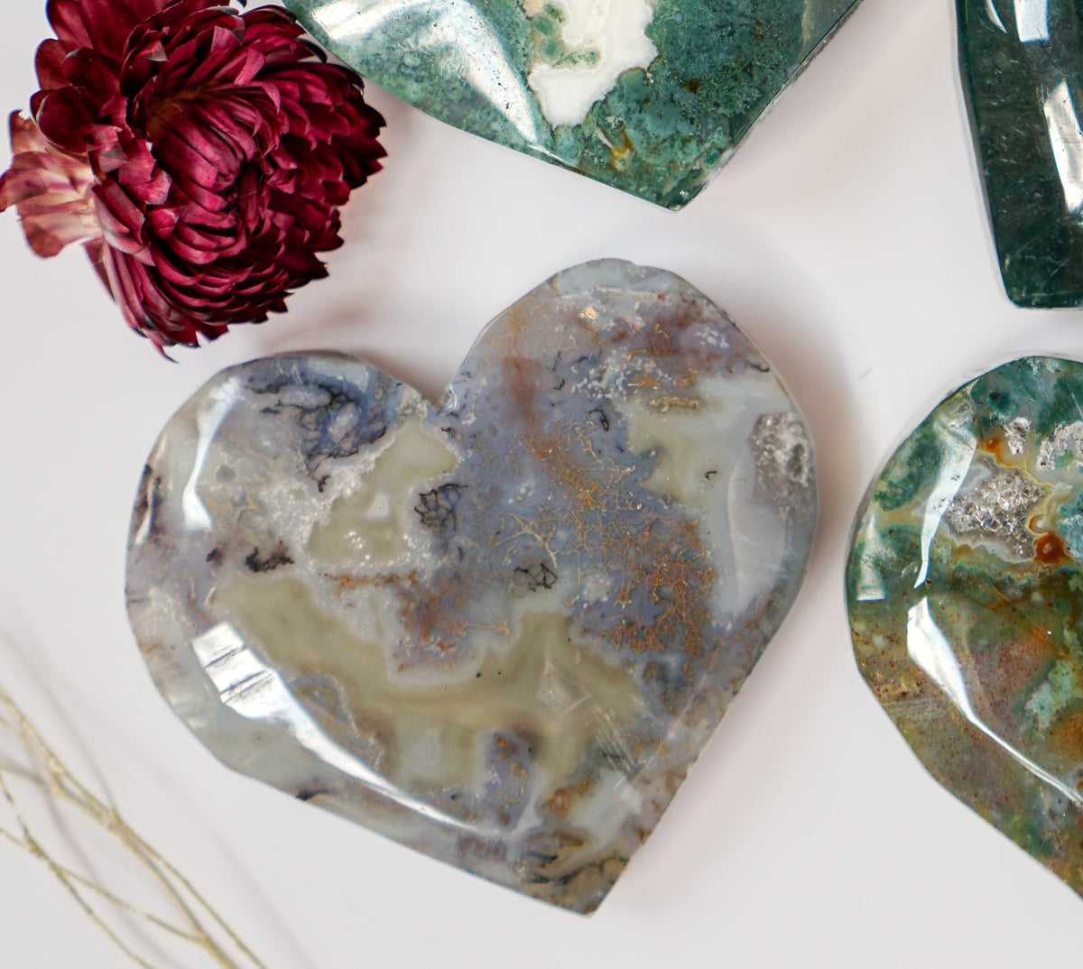 Grey and amber moss agate heart carving with a deep forest green moss agate heart behind it