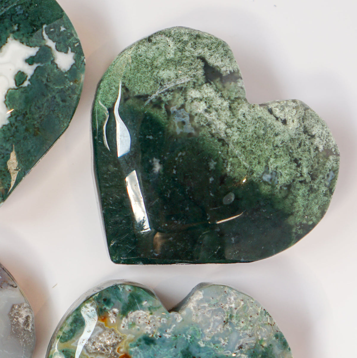 Three moss agate heart carvings arranged together with the deep forest green heart in front