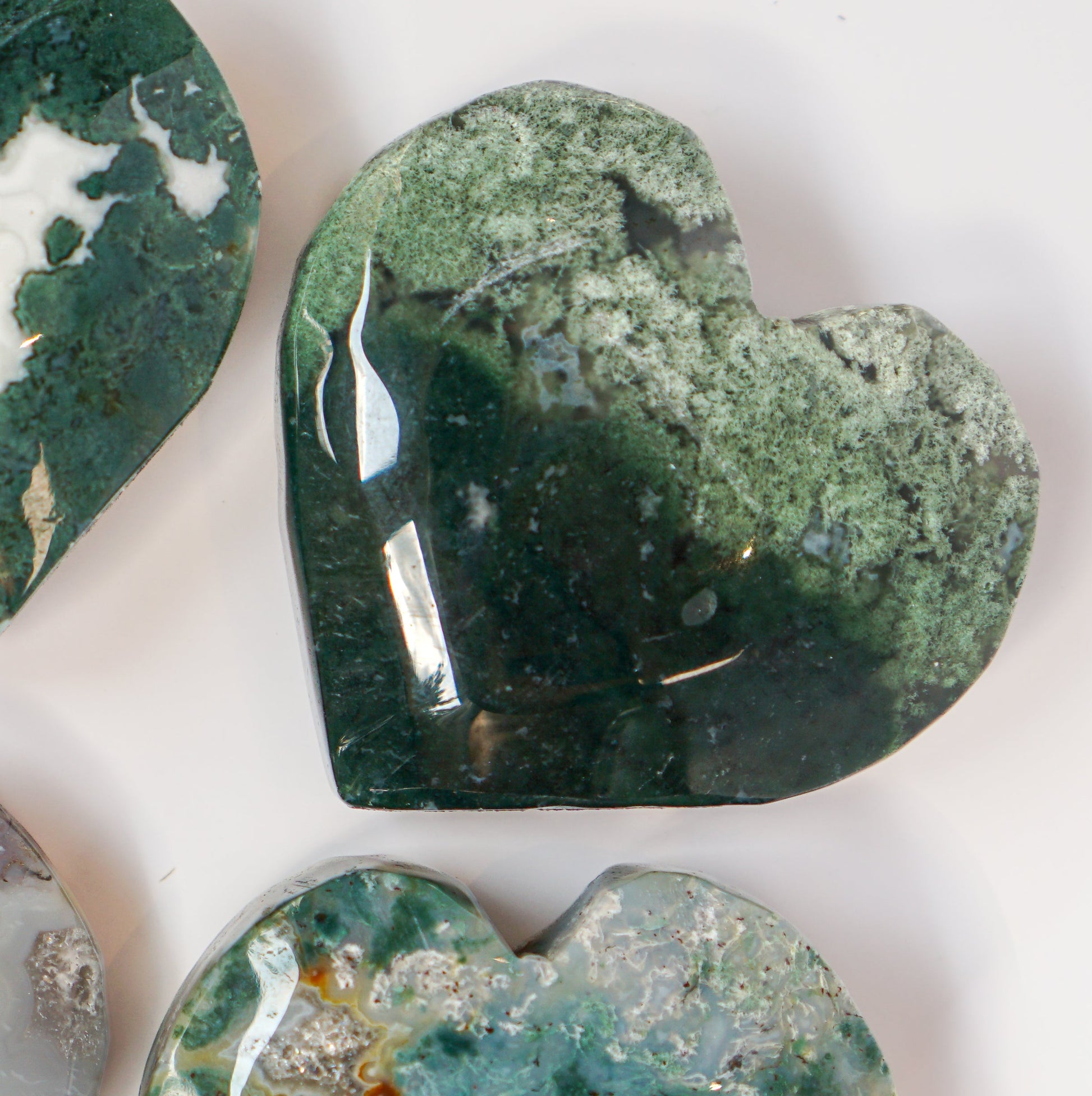 Three moss agate heart carvings arranged together with the deep forest green heart in front
