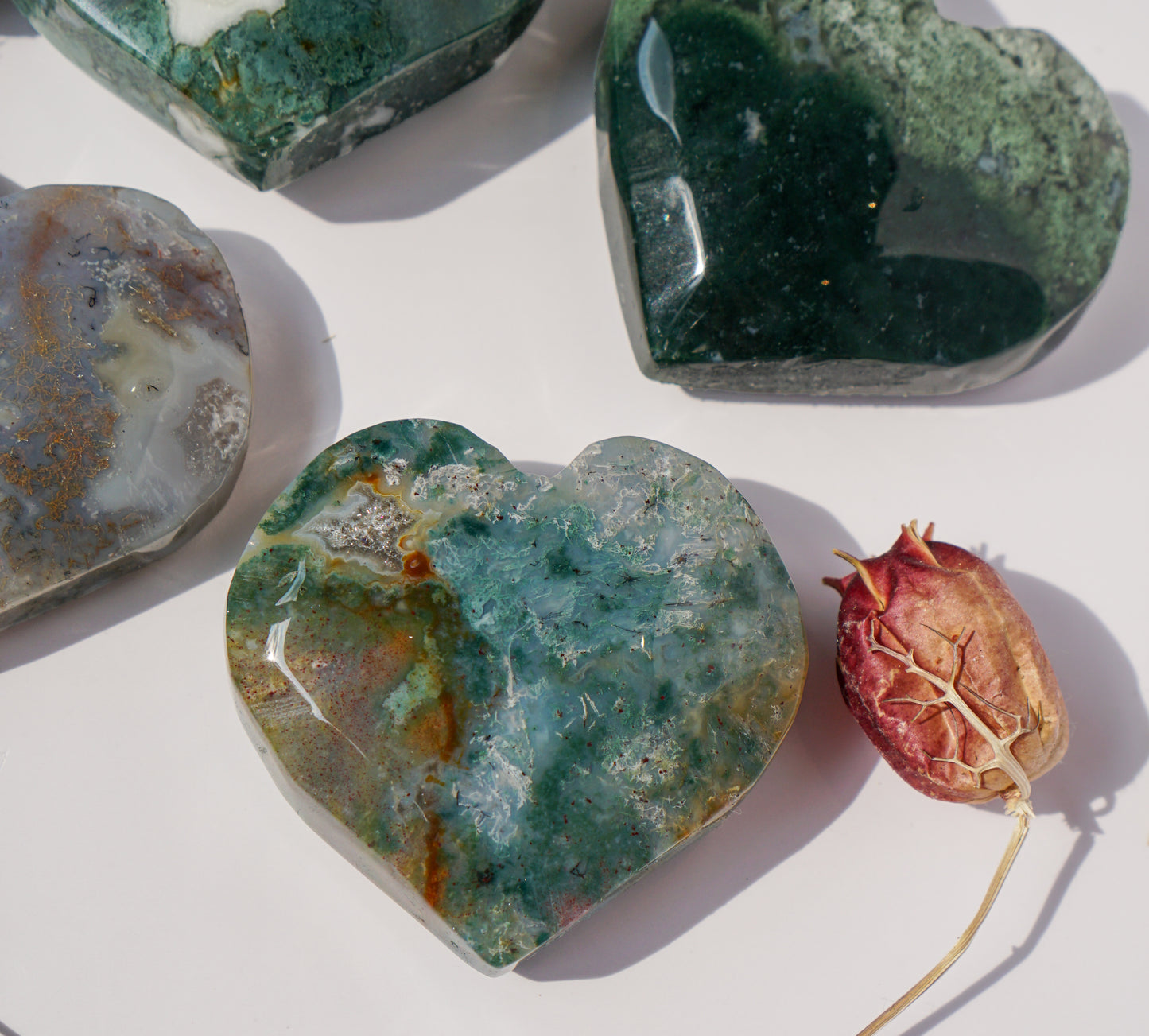 Teal moss agate heart carving in the foreground with a deep forest green moss agate heart behind it