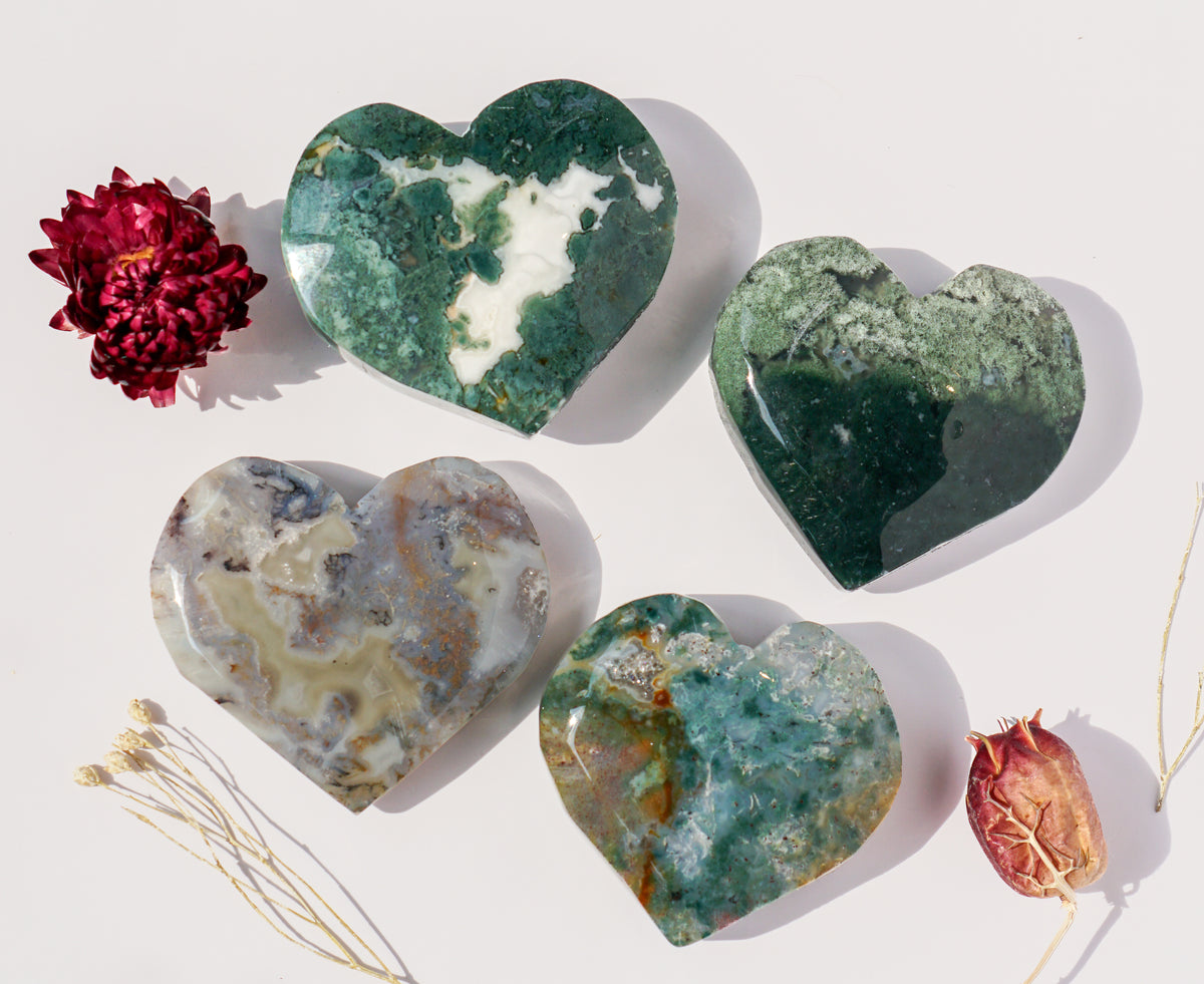 Four moss agate heart carvings in different colors arranged with dried flowers