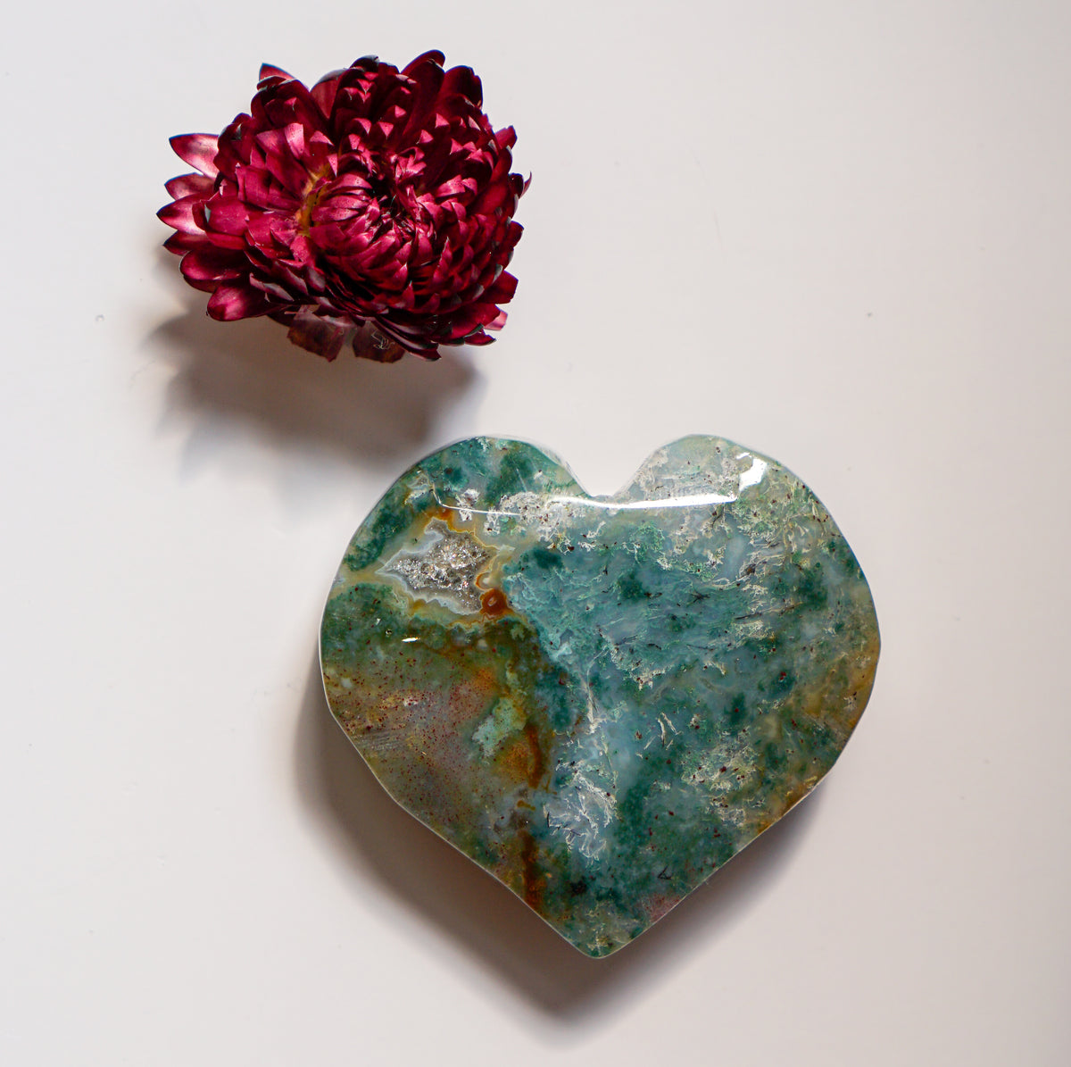 Teal moss agate heart carving with a dried red flower above it