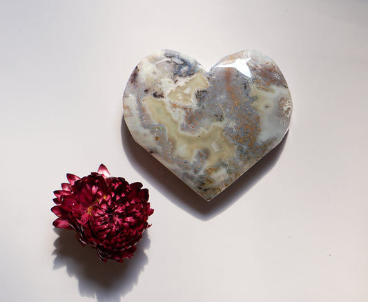 Grey and amber moss agate heart carving beside a dried red flower