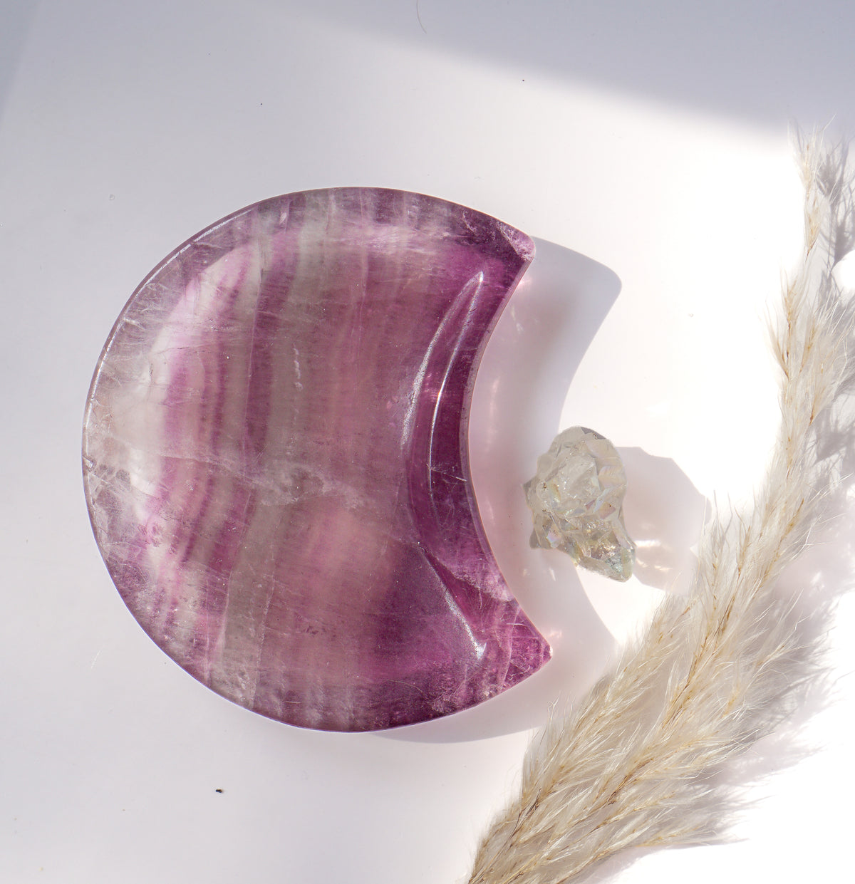 Purple fluorite crescent moon dish with soft lavender and violet banding, styled with a raw quartz point and dried pampas grass in natural light