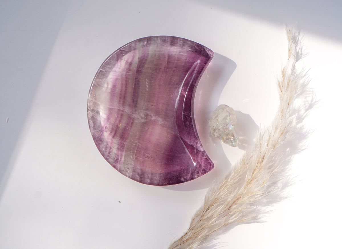 Purple fluorite crescent moon dish with lavender and violet bands, styled with a raw quartz point and dried pampas grass