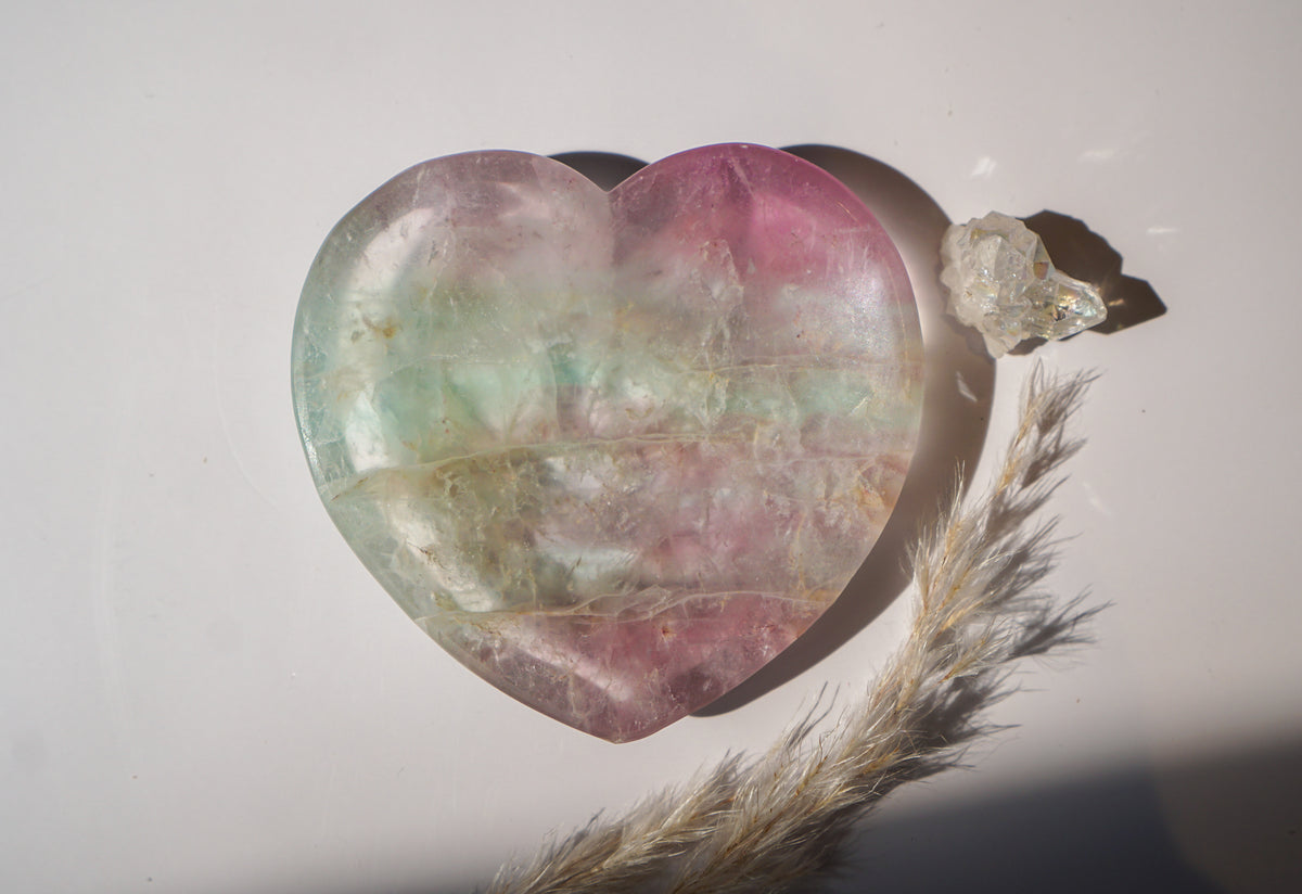 Rainbow fluorite heart dish in soft mint green and blush pink, styled with a raw quartz cluster and dried pampas grass