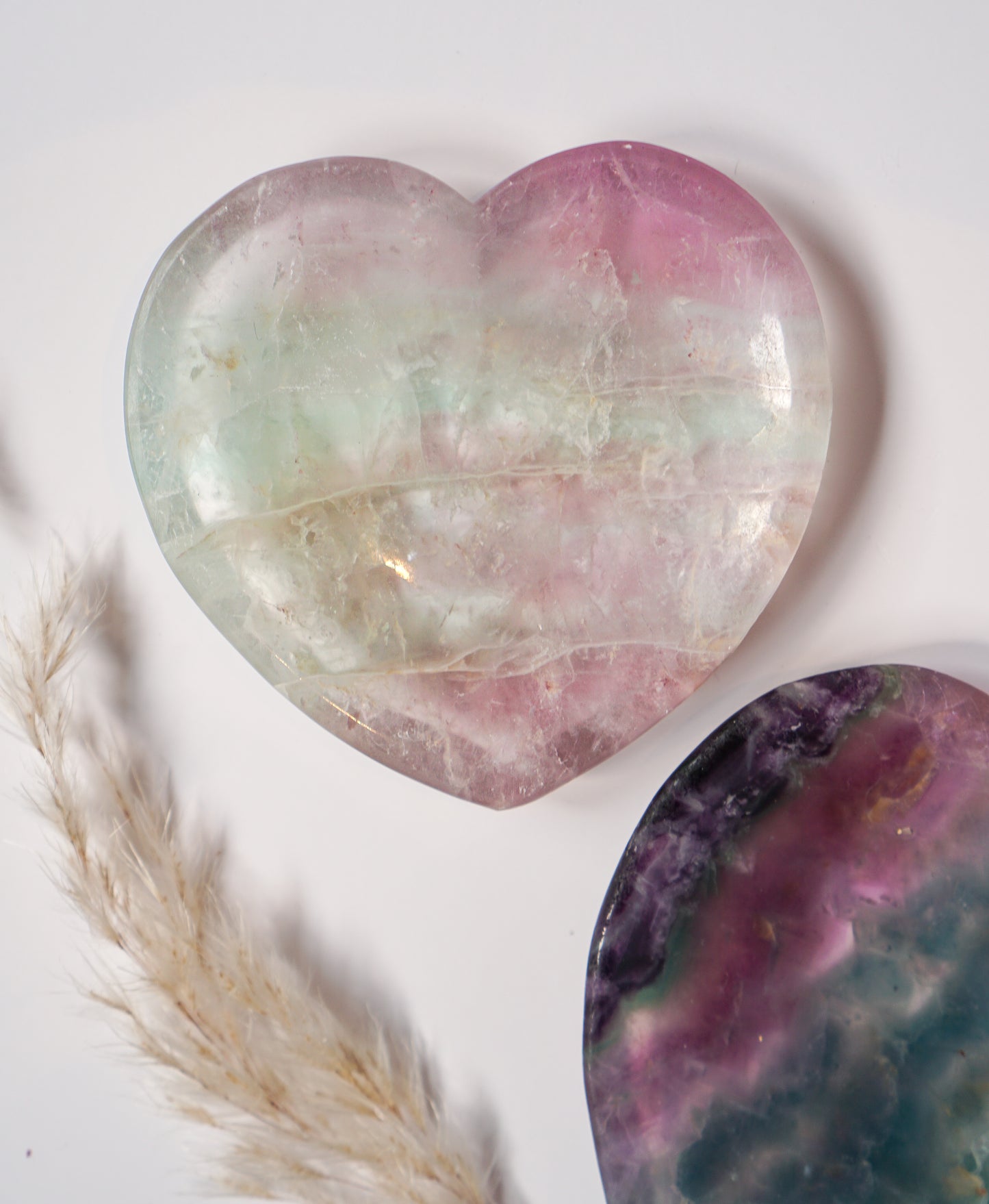 Rainbow fluorite heart dish in soft mint green and blush pink, displayed beside a bold purple, pink, and teal fluorite heart dish