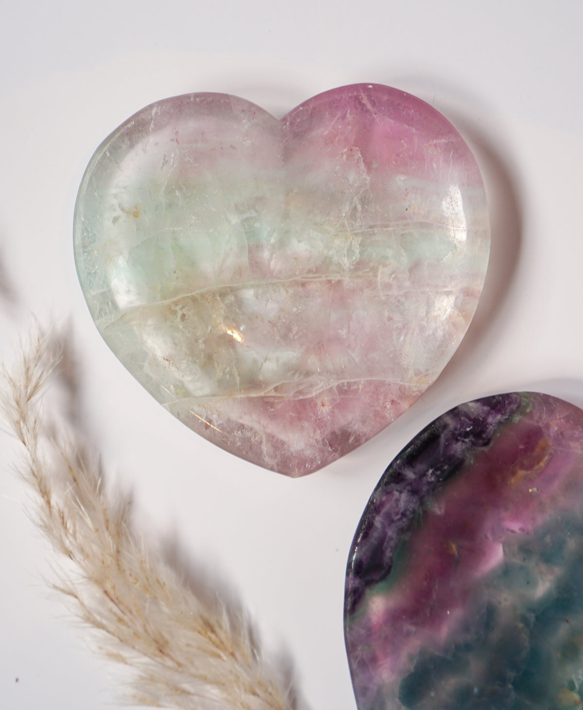 Rainbow fluorite heart dish in soft mint green and blush pink, displayed beside a bold purple, pink, and teal fluorite heart dish