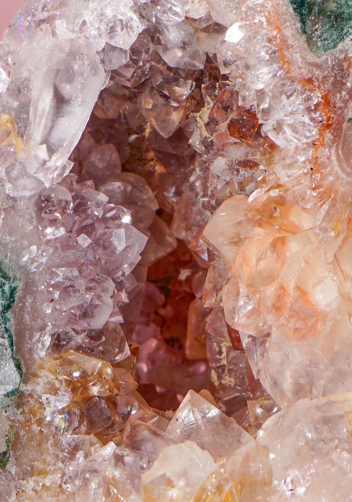 Close-up of a pink amethyst and jasper crystal tower geode specimen with a hollow interior, featuring translucent white and pale pink quartz crystals, peachy orange tones, and hints of green along the outer edges.