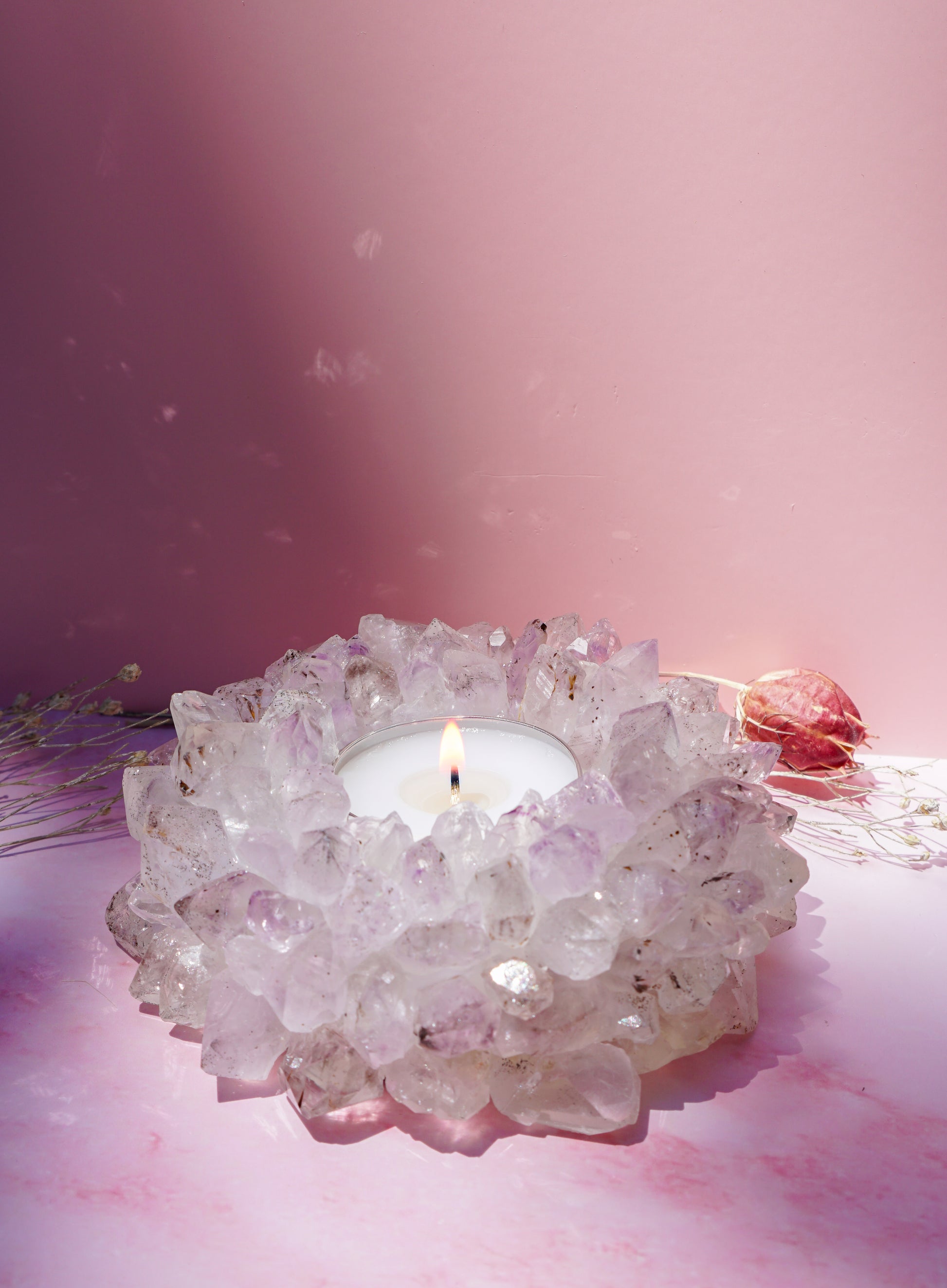 A crystal candle holder druzy brazilian amethyst crystal tea light holder, holding a lit white tea light candle, set against a soft pink background.