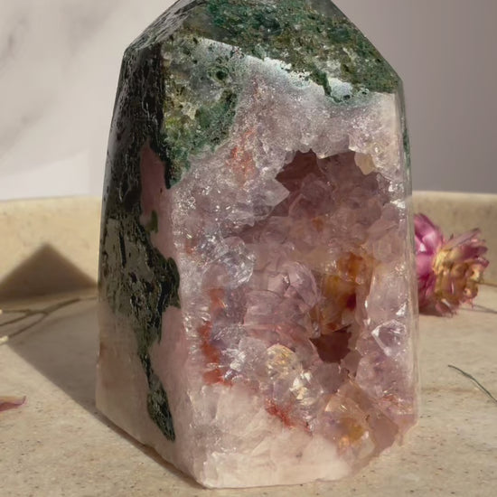 Video of  pink amethyst and jasper crystal tower rotating on beige marble tray with dried flowers