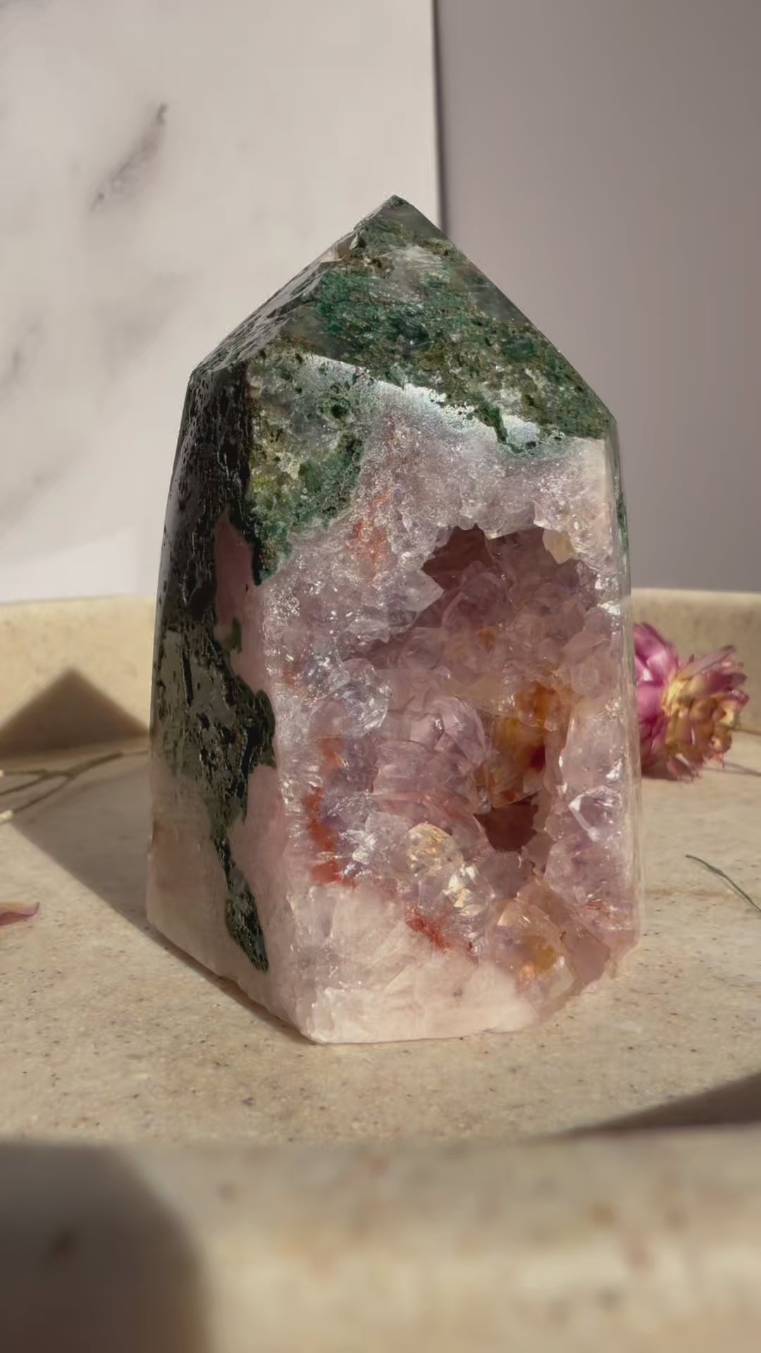 Video of  pink amethyst and jasper crystal tower rotating on beige marble tray with dried flowers